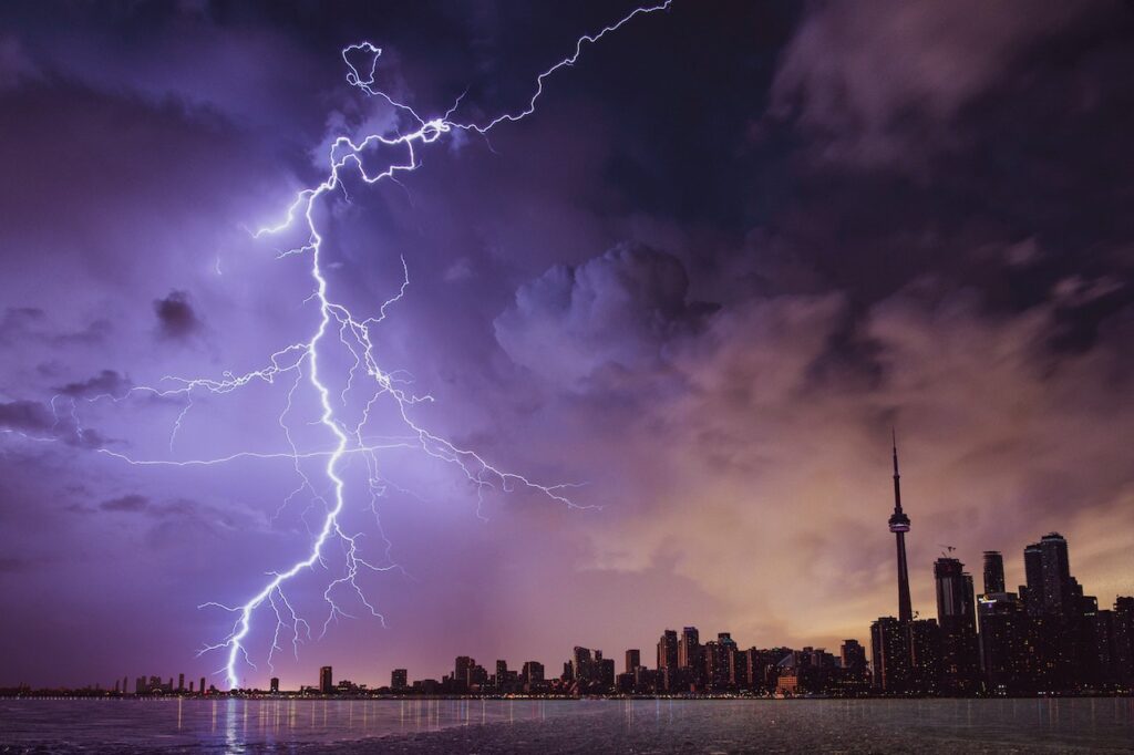 a cityscape at night with purple lightning striking the horizon.