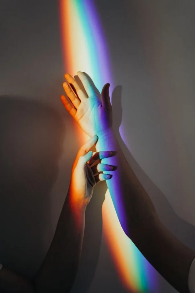 a rainbow reflection of light on two outstretched hands.