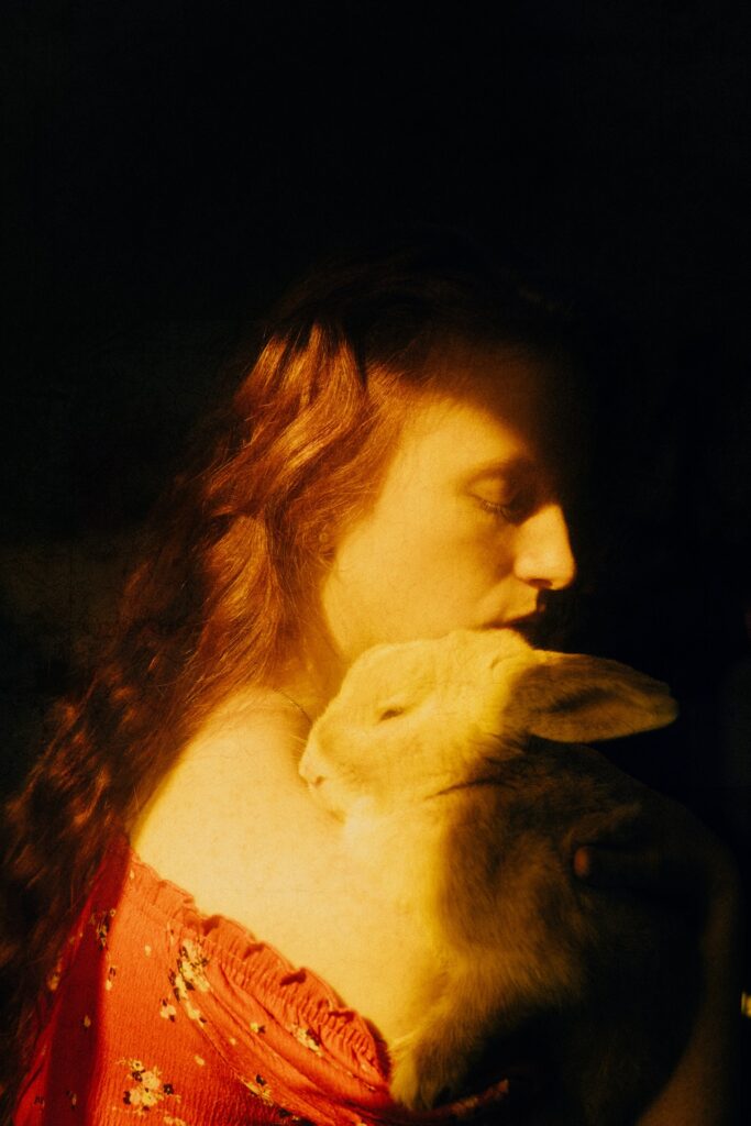 red-haired woman holding a gray rabbit close to her.
