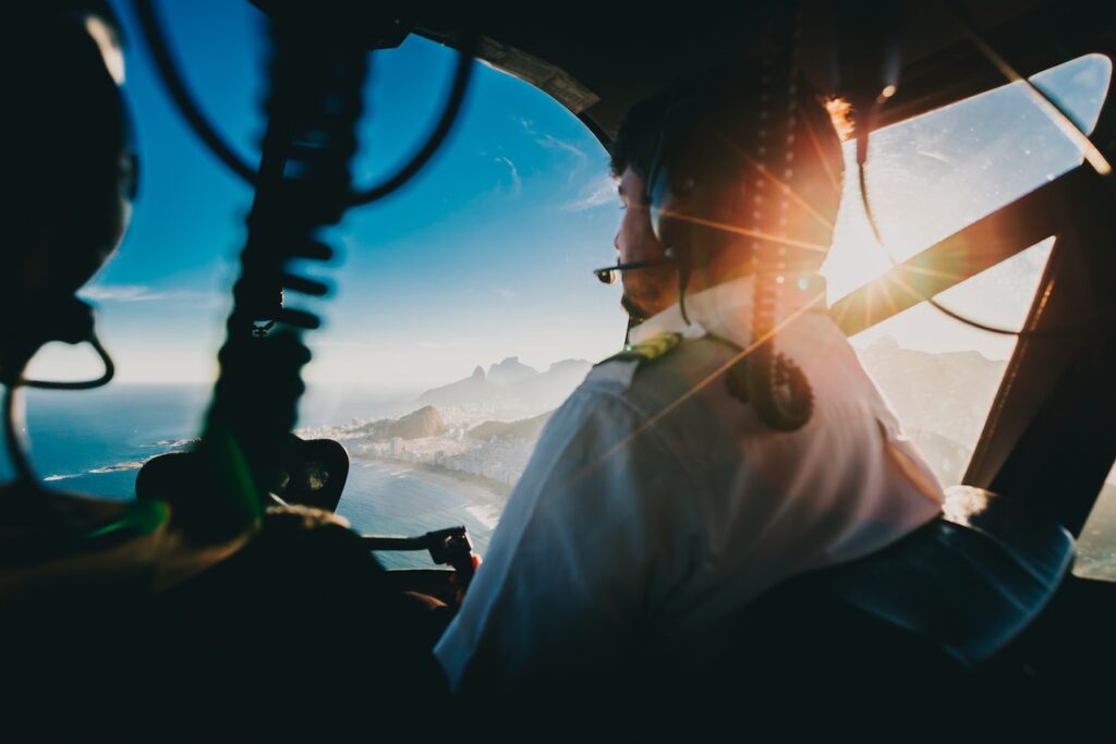 view of two pilots from the backseat of a small aircraft flying over a coastline.