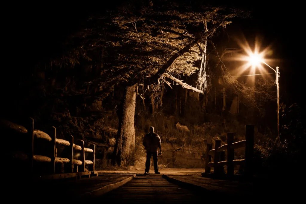 silhouette of a man at the end of a wooden bridge at night lit by one streetlight.