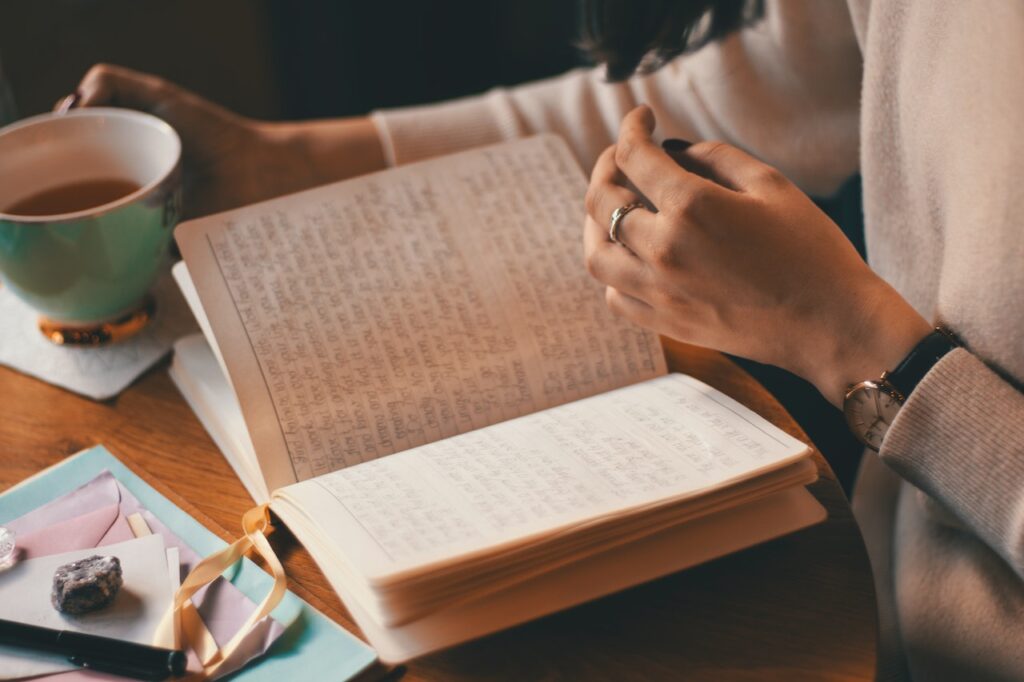 a woman holding a cup of tea and an open journal with handwriting in it.