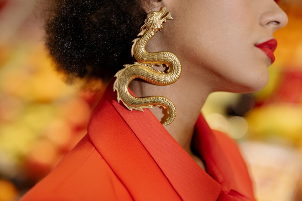 woman in an orange jacket with a golden dragon earring.