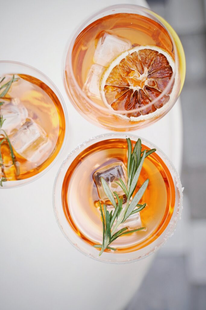 three orange-brown cocktails on a white table seen from above.