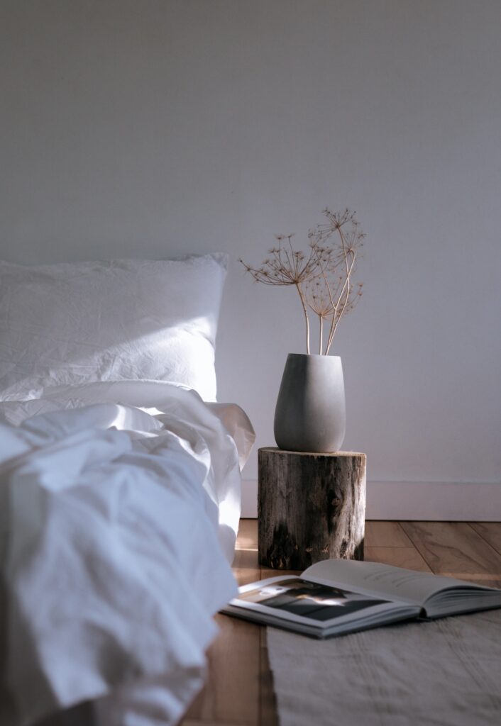 a single stream of sunlight illuminating a gray vase next to a white bed.